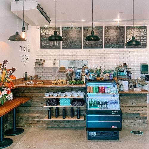 A cozy café interior with a wooden counter, fresh fruits, a drink display, and a menu board overhead.