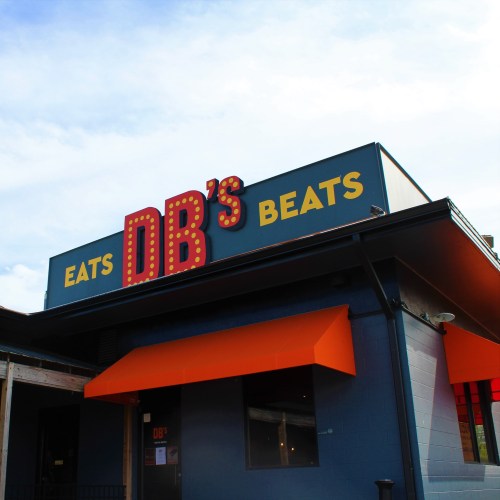 Sign for DB's Eats Beats on a building with an orange awning under a blue sky.