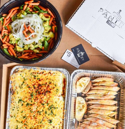 A colorful salad with carrots and greens, a box of baked pasta, and lemon wedges on a cardboard background.