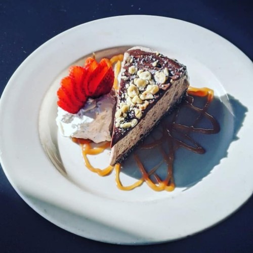 A slice of chocolate mousse cake topped with nuts, served with whipped cream and strawberries on a white plate.