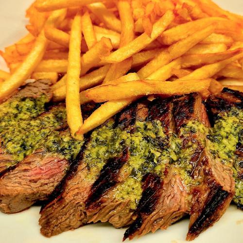 Grilled steak slices topped with green sauce, served alongside a generous portion of golden French fries.