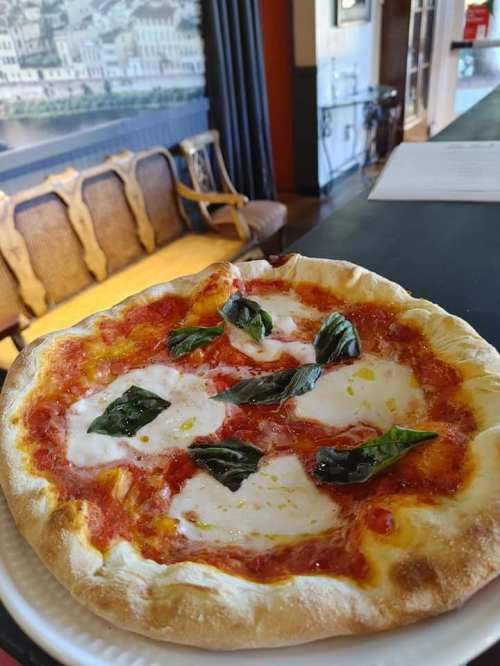 A freshly baked pizza topped with mozzarella cheese and basil leaves, served on a white plate in a cozy setting.