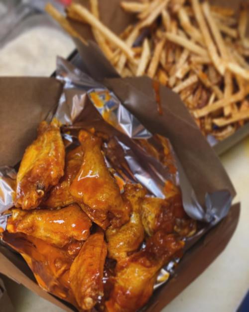A box of saucy chicken wings next to a container of golden French fries.