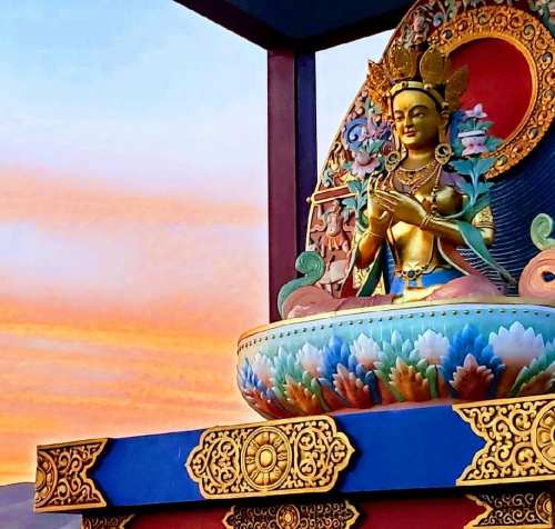 A colorful statue of a seated Buddha against a vibrant sunset sky.