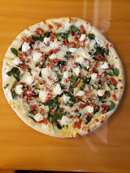 A round pizza topped with spinach, cheese, and bits of bacon on a wooden table.