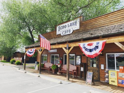 A rustic café with a wooden exterior, American flags, and patriotic decorations, surrounded by trees and parked cars.