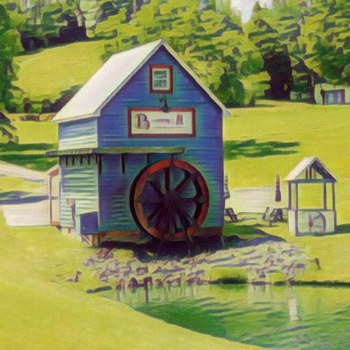 A blue watermill with a large wheel, set in a green landscape with a pond and picnic area nearby.