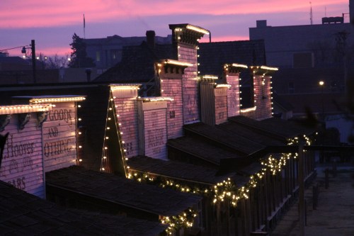 Historic buildings adorned with festive lights against a colorful sunset sky.