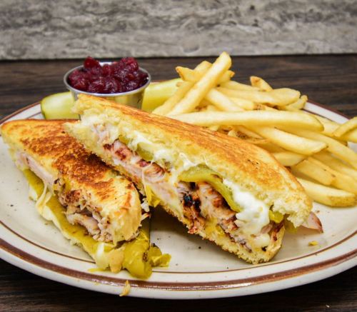 A grilled sandwich with chicken and pickles, served with fries and a small bowl of cranberry sauce.