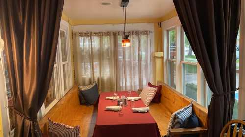 Cozy dining area with a red tablecloth, surrounded by curtains and cushions, featuring a warm pendant light.