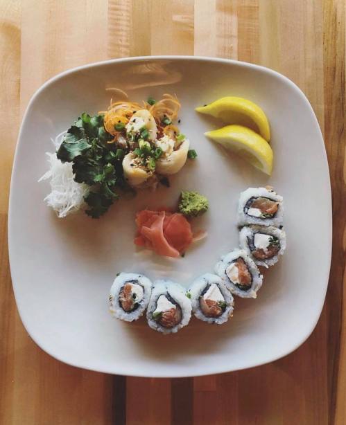 A plate of sushi rolls with ginger, wasabi, salad, and lemon wedges on a wooden table.