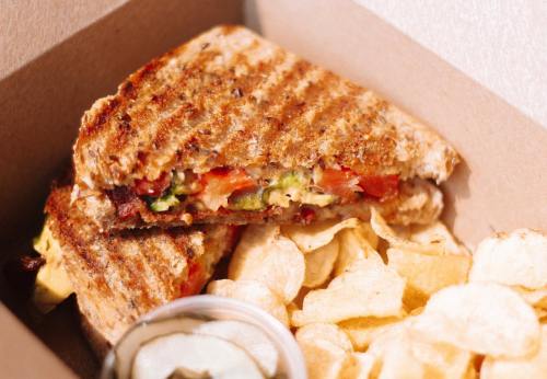 A grilled sandwich with vegetables and cheese, served with potato chips and a small container of dipping sauce.