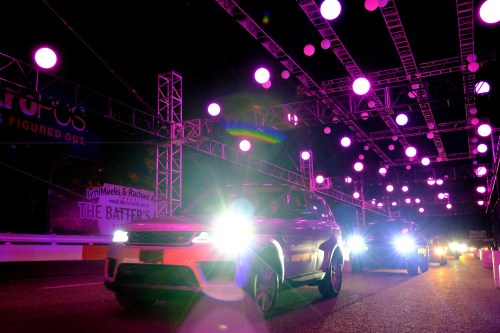 Cars drive under colorful lights at night, with a vibrant display of pink and purple hanging decorations above.