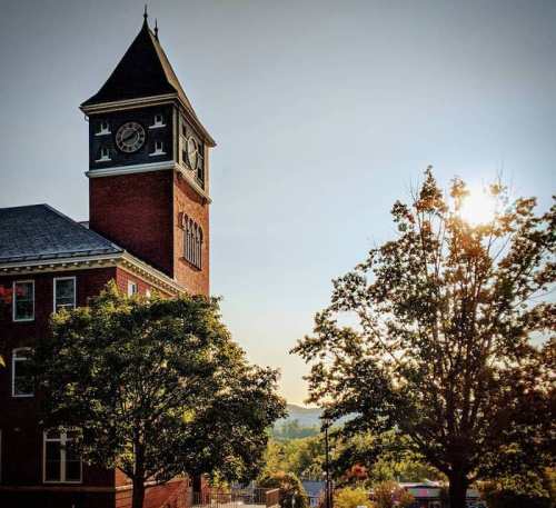Historic clock tower at sunset, surrounded by trees and a clear sky.