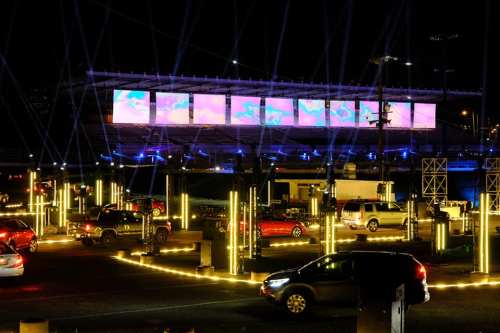 A nighttime scene of a stadium with colorful lights and vehicles parked around, creating a vibrant atmosphere.