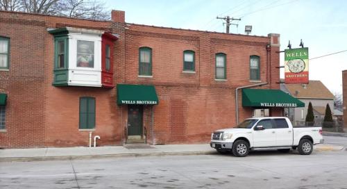 Brick building with green and red accents, featuring a sign for "Wells Brothers" and a parked white pickup truck.