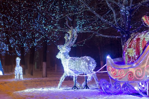 A glowing reindeer and a colorful sleigh adorned with lights, set against a backdrop of twinkling blue lights in a snowy scene.