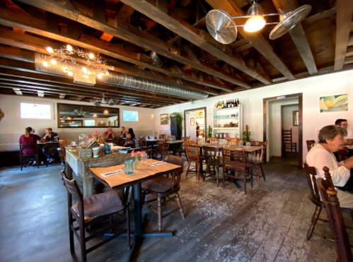Cozy restaurant interior with wooden beams, tables set for dining, and patrons enjoying their meals.