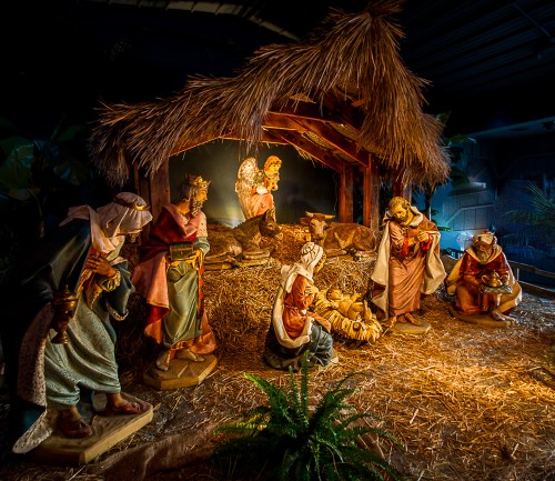 Nativity scene with figures of Mary, Joseph, and the Three Wise Men around a manger, illuminated with soft lighting.