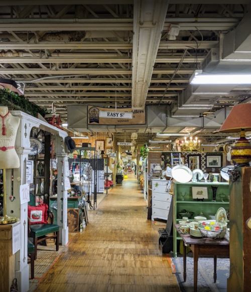 A spacious antique shop aisle lined with various vintage items and displays, illuminated by overhead lights.