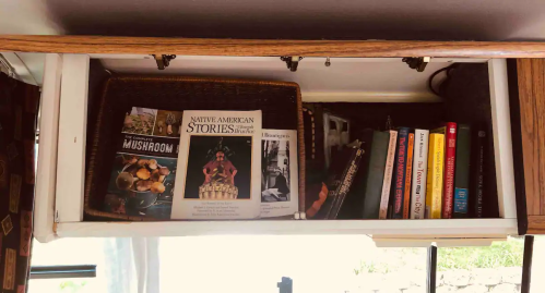 A wooden shelf with books and a basket, featuring titles on mushrooms and Native American stories.