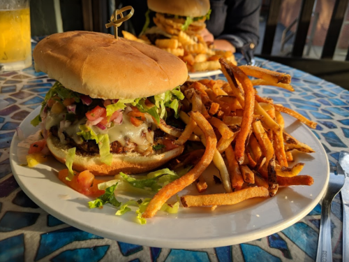 A large burger topped with lettuce, tomatoes, and sauce, served with a side of crispy sweet potato fries.