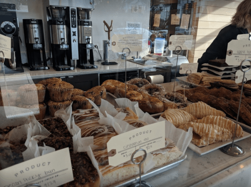 A display case filled with various baked goods, including muffins, pastries, and cinnamon rolls, with coffee machines in the background.