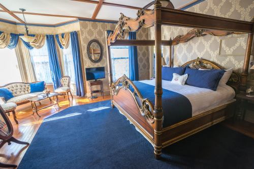 Elegant bedroom featuring a four-poster bed, vintage furniture, and rich blue accents in a beautifully decorated space.