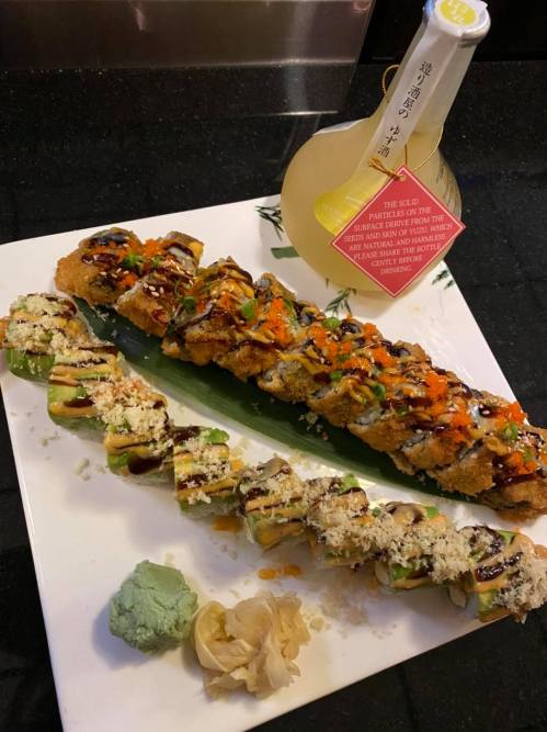 A plate of sushi rolls with various toppings, wasabi, pickled ginger, and a bottle of drink in the background.