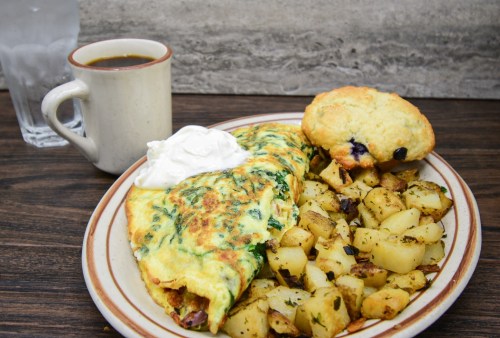 A plate with a spinach omelette, seasoned potatoes, a biscuit, and a cup of coffee beside a glass of water.