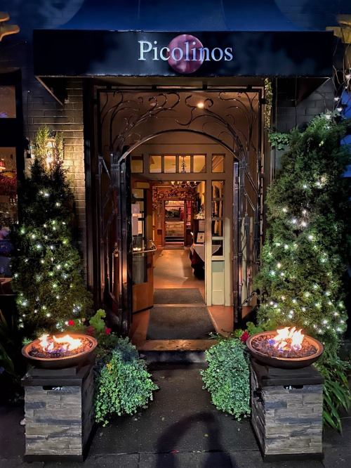 Entrance of Picolinos restaurant, featuring decorative plants, glowing lights, and fire pits on either side.