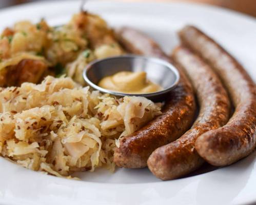 A plate featuring three sausages, a side of sauerkraut, and a small bowl of mustard.