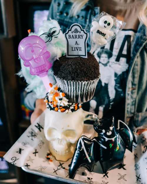 A spooky dessert display featuring a cupcake on a skull, decorated with candy and Halloween-themed toppers.