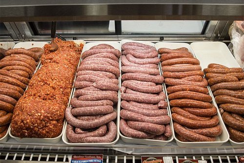 A display of various types of sausages arranged in trays, including links and a large meatloaf.