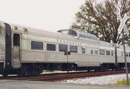 A vintage Tennessee Central train with a streamlined design, parked near a railroad crossing sign.