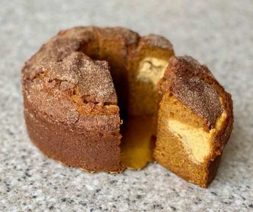 A round cake with a cinnamon-sugar topping, partially sliced to reveal a creamy filling inside.
