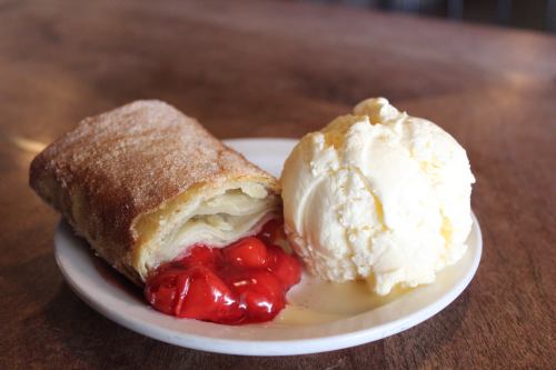 A slice of cherry strudel dusted with sugar, served with a scoop of vanilla ice cream on a white plate.