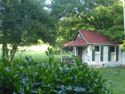 A quaint, weathered house with a red roof, surrounded by greenery and trees in a peaceful rural setting.