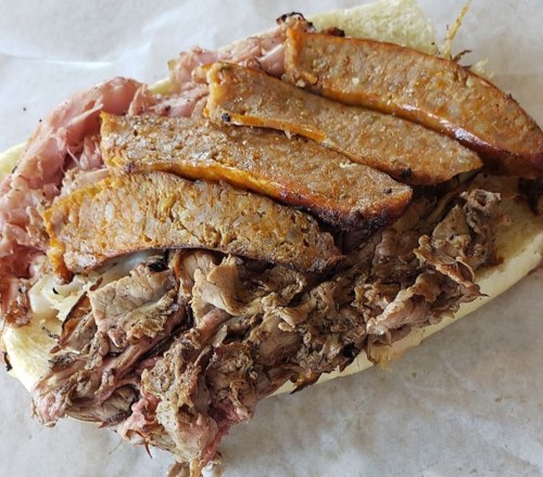 A sandwich filled with layers of sliced meats, including brisket and sausage, on a soft hoagie roll.