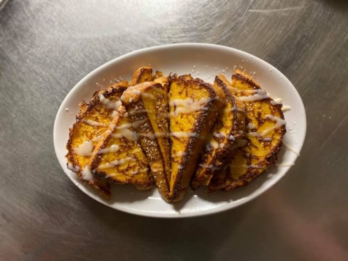 A plate of golden-brown French toast slices drizzled with icing, arranged neatly on a white dish.