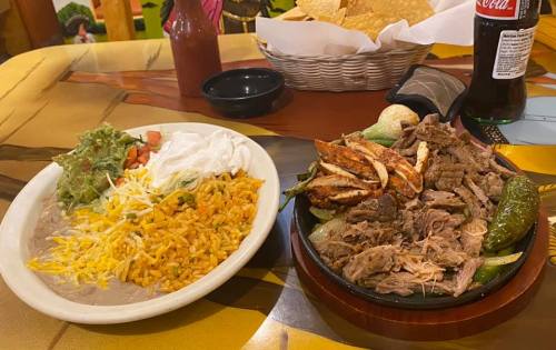 A plate of rice, beans, guacamole, and sour cream next to a sizzling platter of grilled meats and jalapeños.
