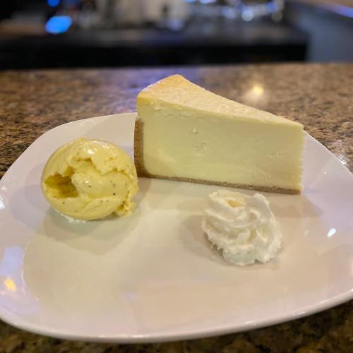 A slice of cheesecake on a plate, accompanied by a scoop of vanilla ice cream and a dollop of whipped cream.