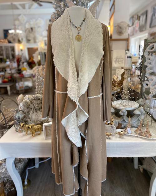 A cozy, beige wrap with a fluffy white collar displayed on a mannequin in a decorated shop.