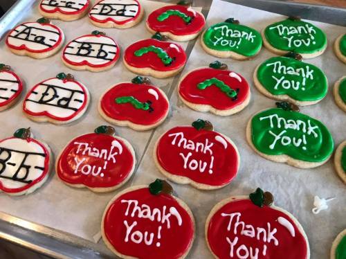 A tray of decorated cookies shaped like apples, featuring red and green icing with "Thank You!" written on them.