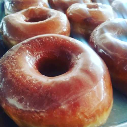 A close-up of glazed donuts arranged on a tray, showcasing their shiny, golden-brown surface.