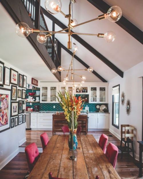 A modern dining area with a wooden table, stylish light fixtures, and a bright kitchen in the background.