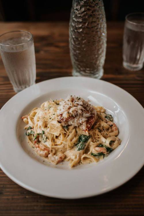 A plate of creamy pasta with shrimp and spinach, topped with grated cheese, served with two glasses of water.