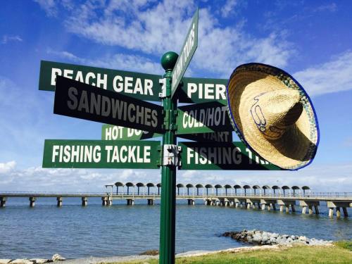 A signpost with directional arrows for various activities, featuring a sombrero hanging on one of the signs by the water.