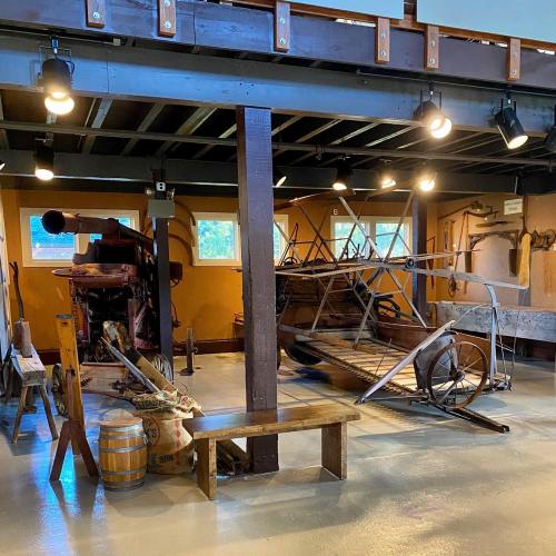 Interior of a museum displaying vintage farming equipment and tools, with wooden beams and warm lighting.