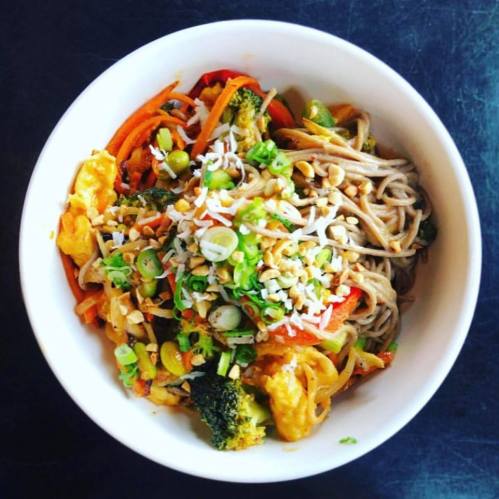 A bowl of soba noodles topped with colorful vegetables, peanuts, and green onions.